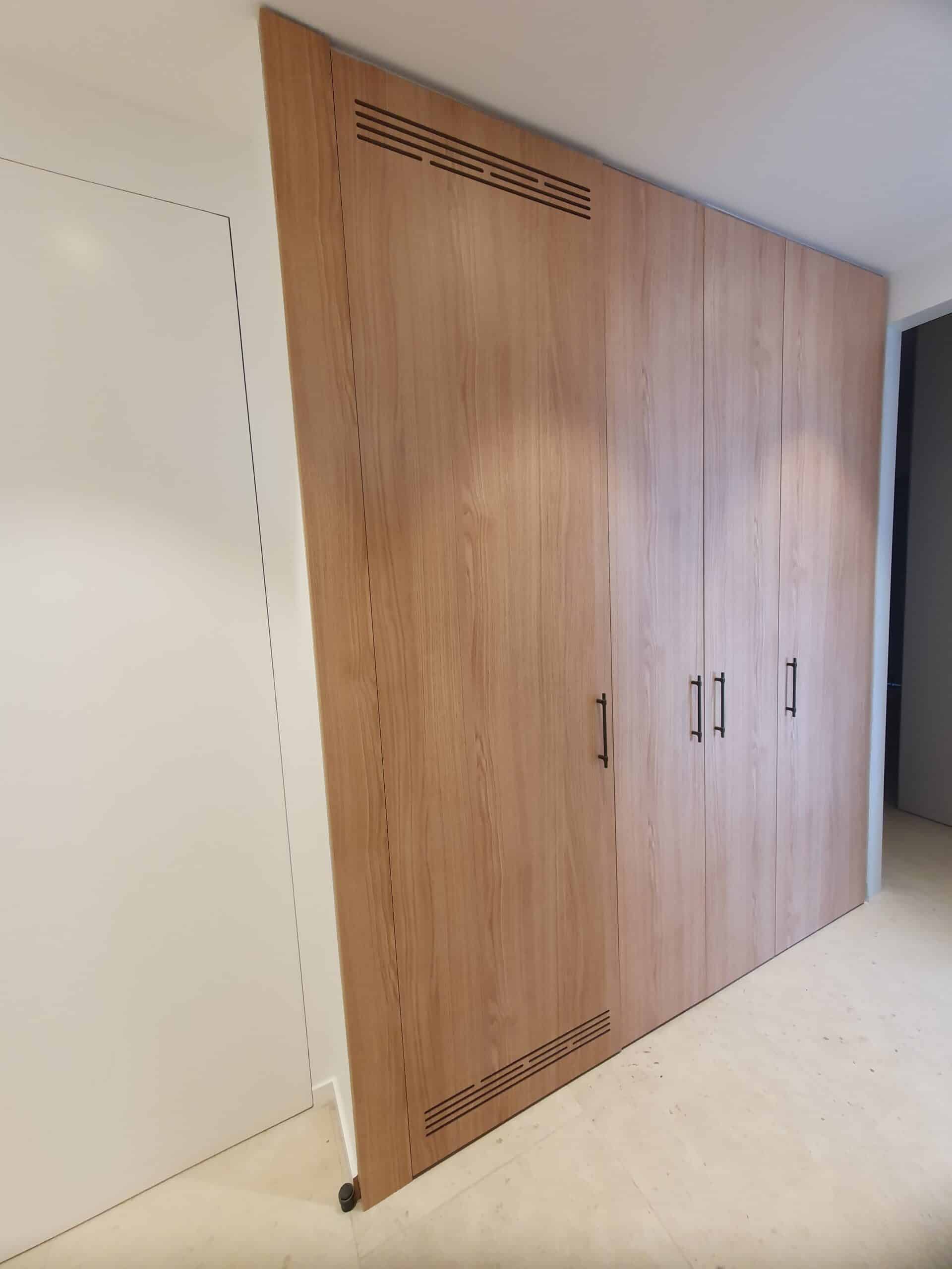 Placard intégré en bois clair avec poignées noires et grilles d'aération horizontales.