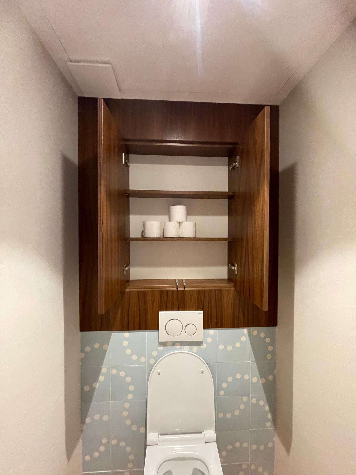 WC blanc sous placard bois ouvert avec papier toilette, carrelage bleu à motifs pois blancs dans toilettes modernes.