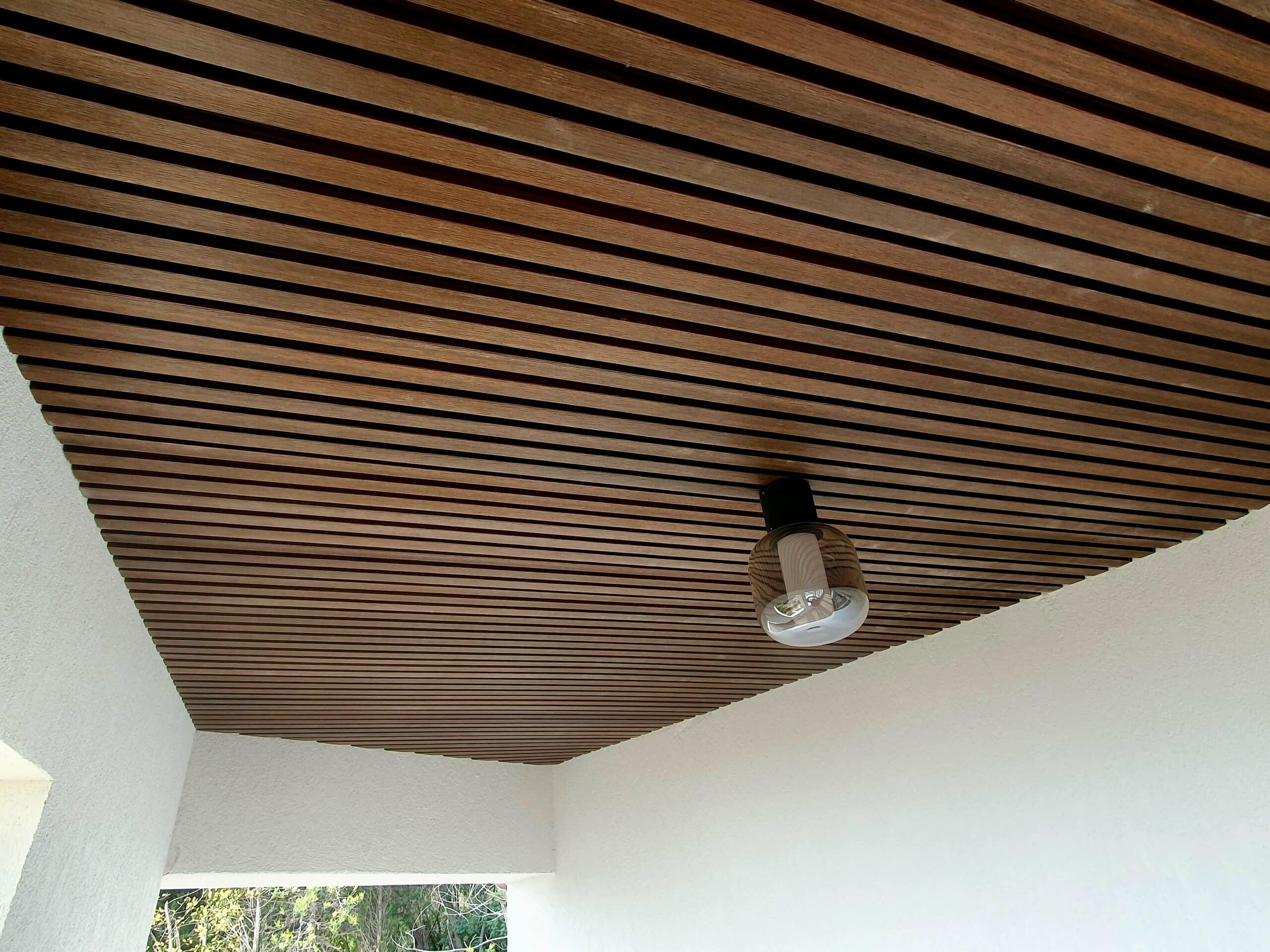Plafond en lattes de bois avec luminaire moderne et murs blancs.