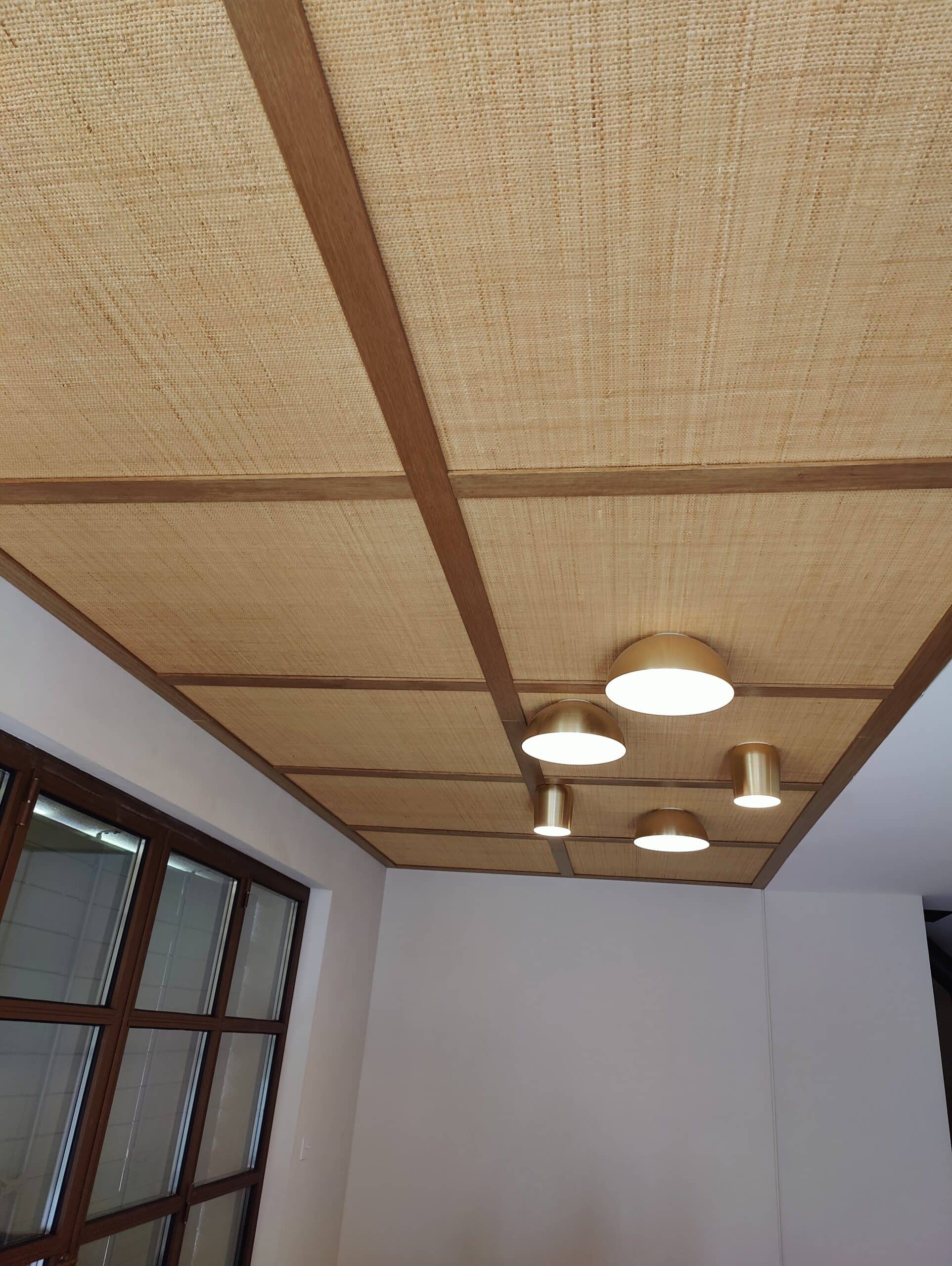Plafond en paille tissée, poutres en bois et suspension de luminaires dorés modernes.