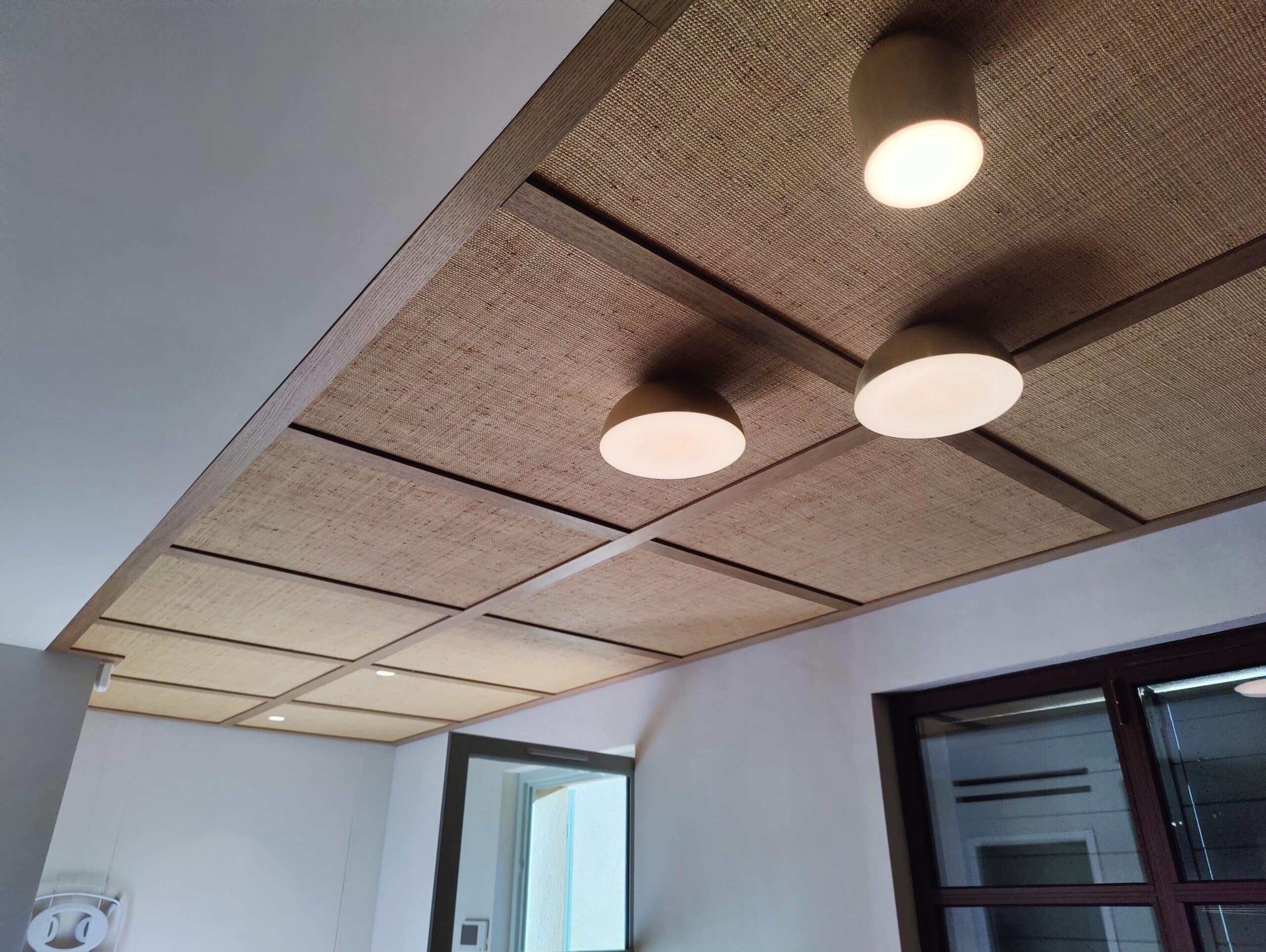 Plafond en rotin à caissons et luminaires ronds, design naturel et moderne.