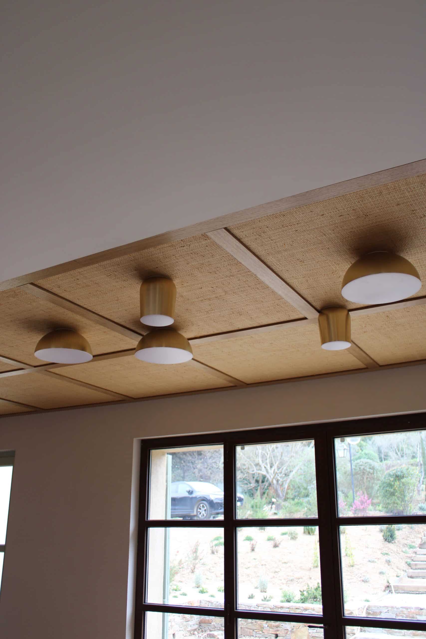 Plafonniers en laiton sur plafond en jute tressée et bois, éclairage design moderne avec vue sur jardin.