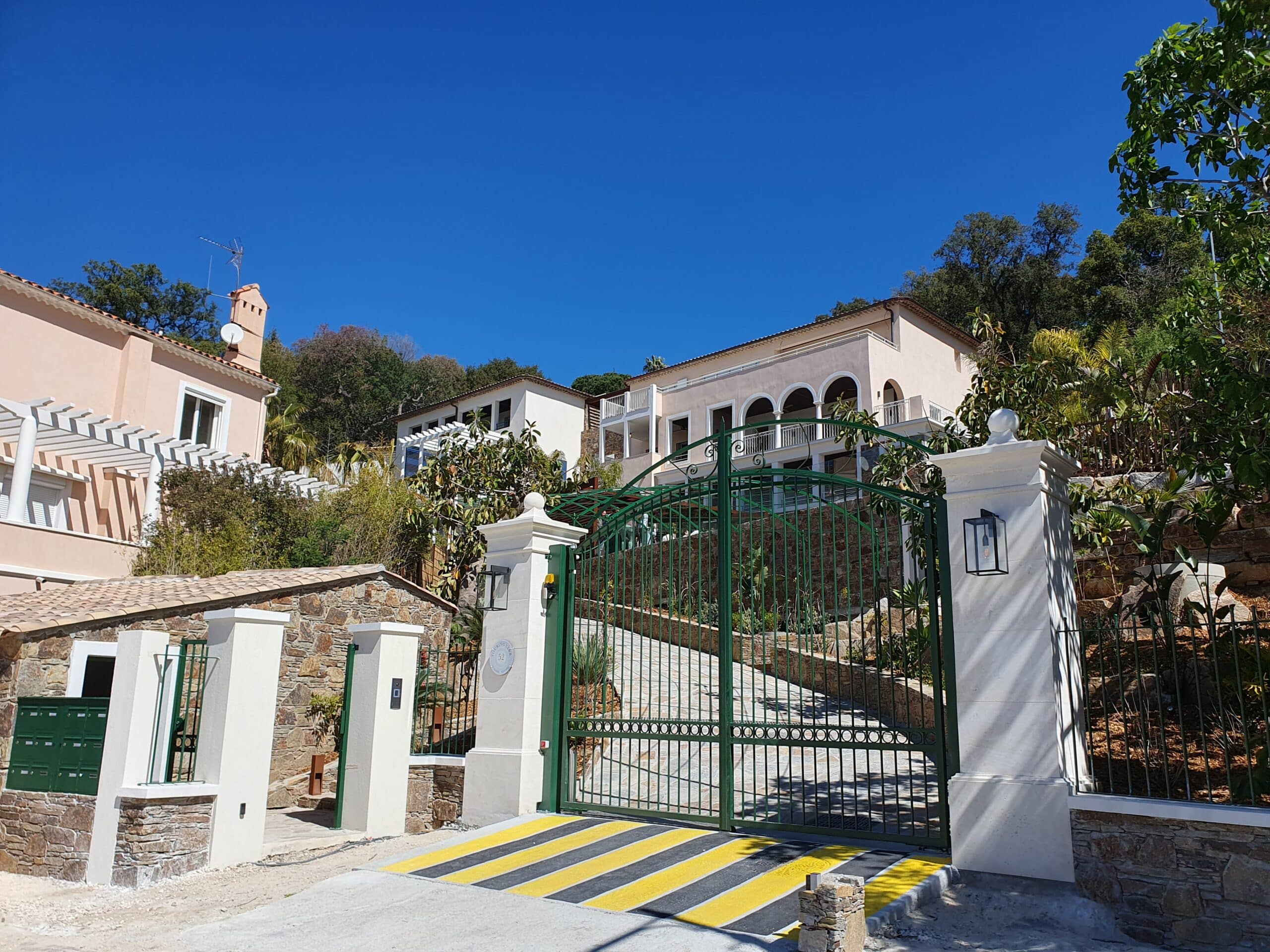 Grand portail vert devant une villa méditerranéenne sous un ciel bleu intense.