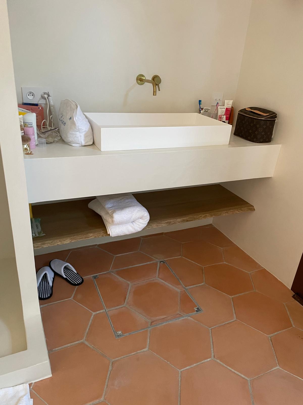 Vasque blanche, robinet doré et sol en tomettes dans une salle de bain au style minimaliste.