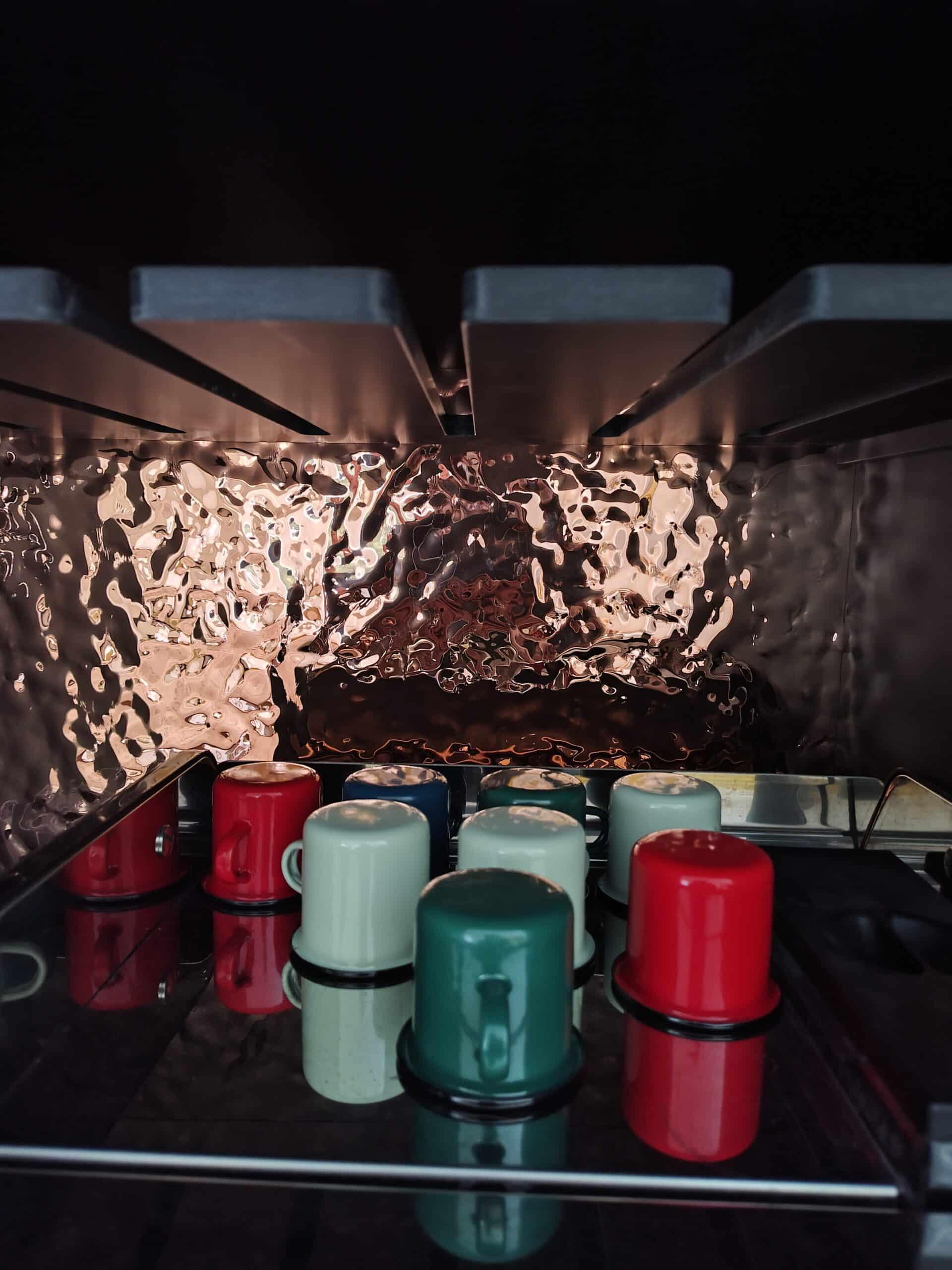 Petites tasses émaillées colorées sur surface réfléchissante et paroi métallique martelée.