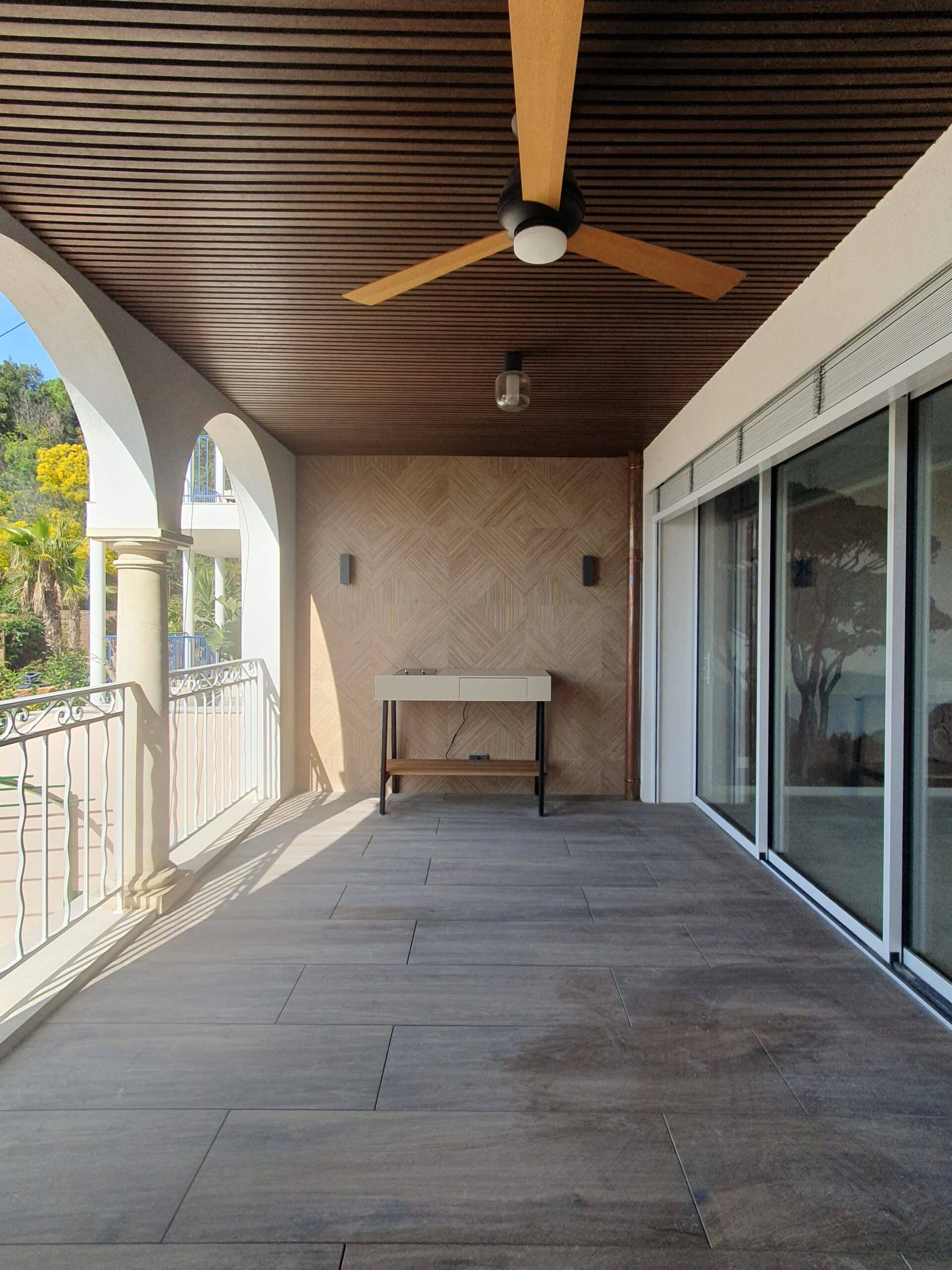 Terrasse moderne avec arches blanches, plafond en bois, ventilateur et grandes baies vitrées coulissantes.
