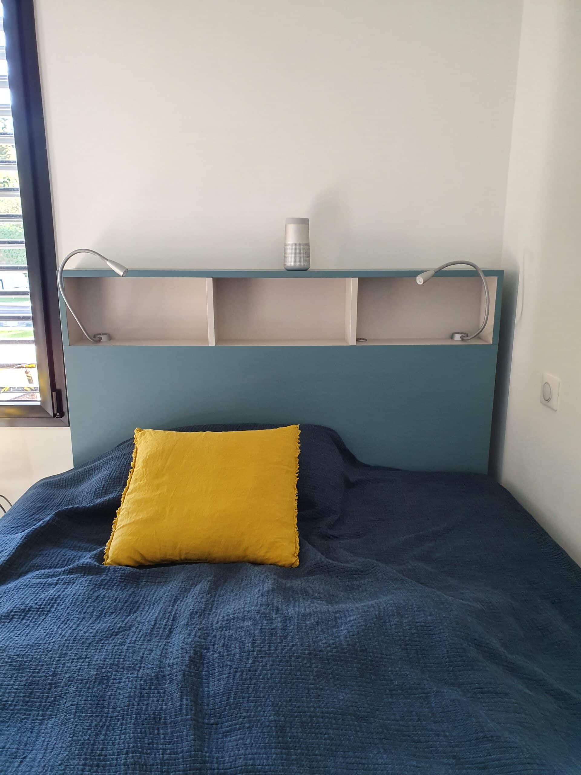 Tête de lit bleue avec étagères, lampes et coussin jaune sur lit marine.