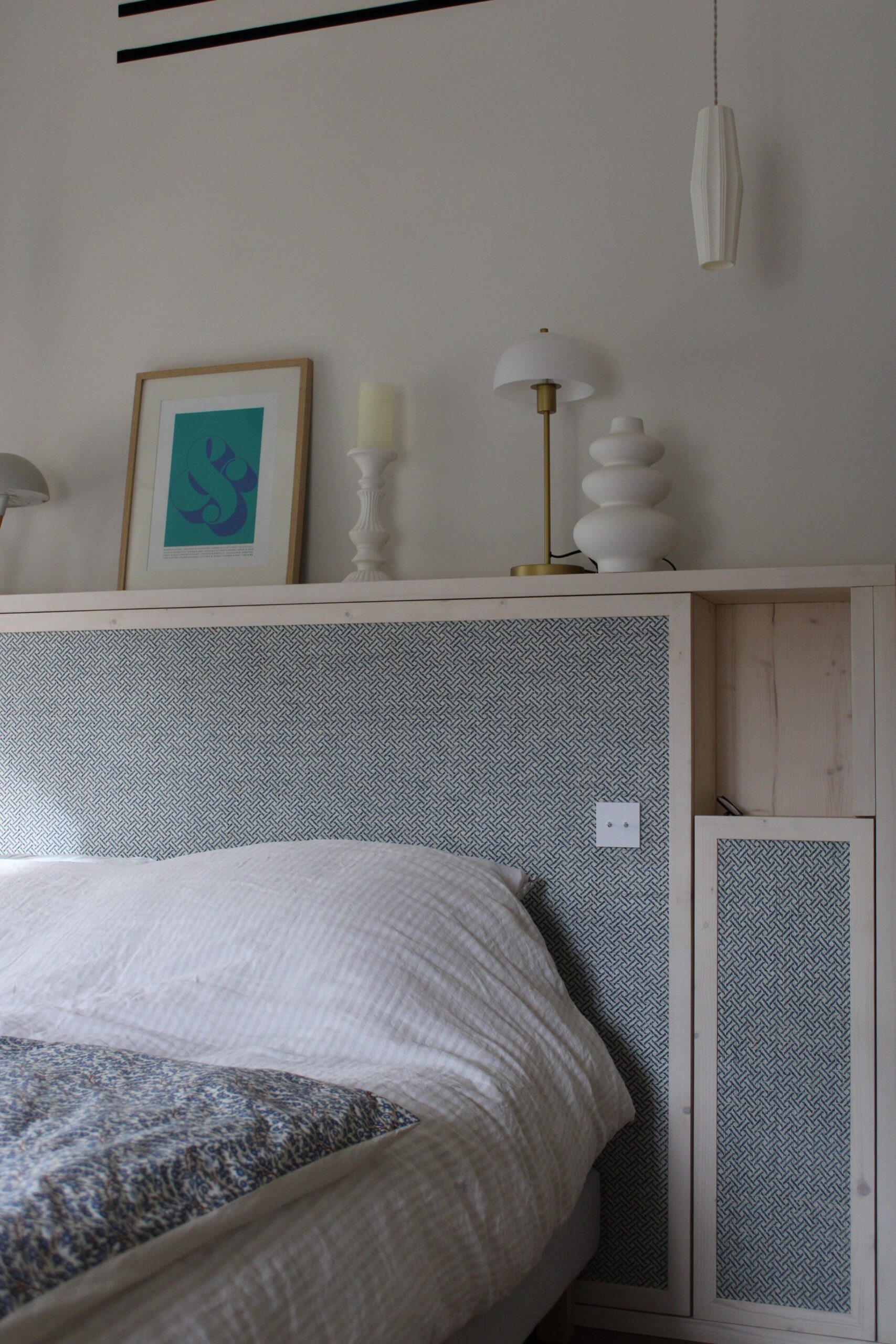 Lit avec tête de lit bois clair, motif bleu géométrique, lampe champignon et cadre décoratif sur étagère.