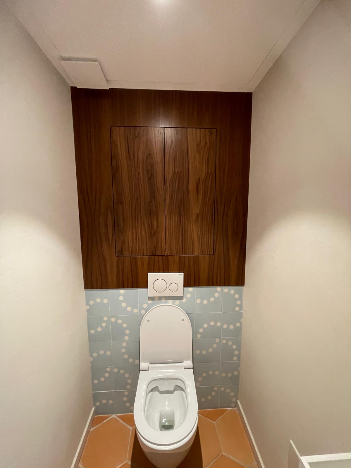 Toilette suspendue, mur en bois sombre, carrelage bleu à pois et sol en terre cuite.