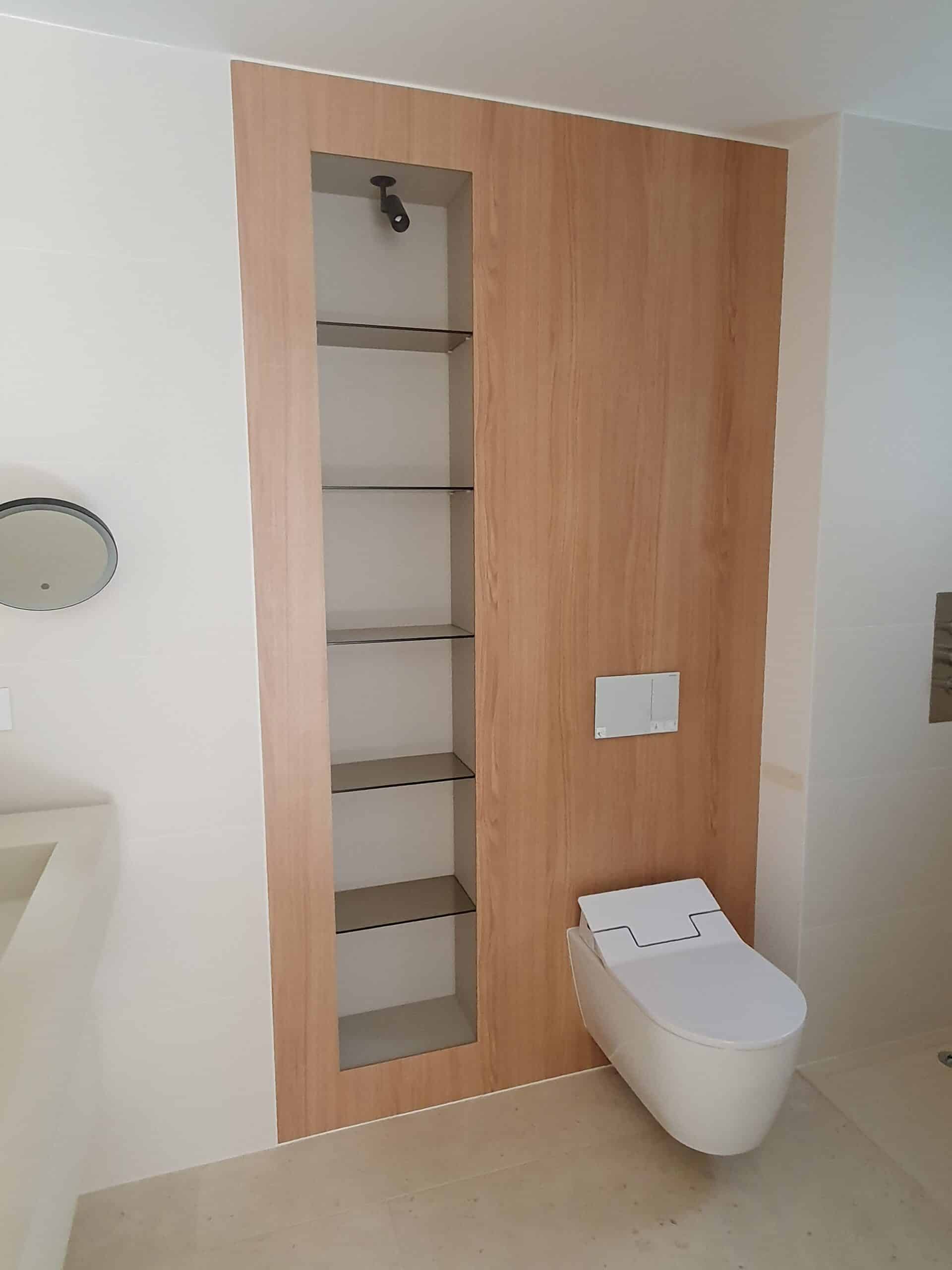 Toilette suspendue sur panneau bois avec étagères en verre encastrées dans une salle de bain épurée.
