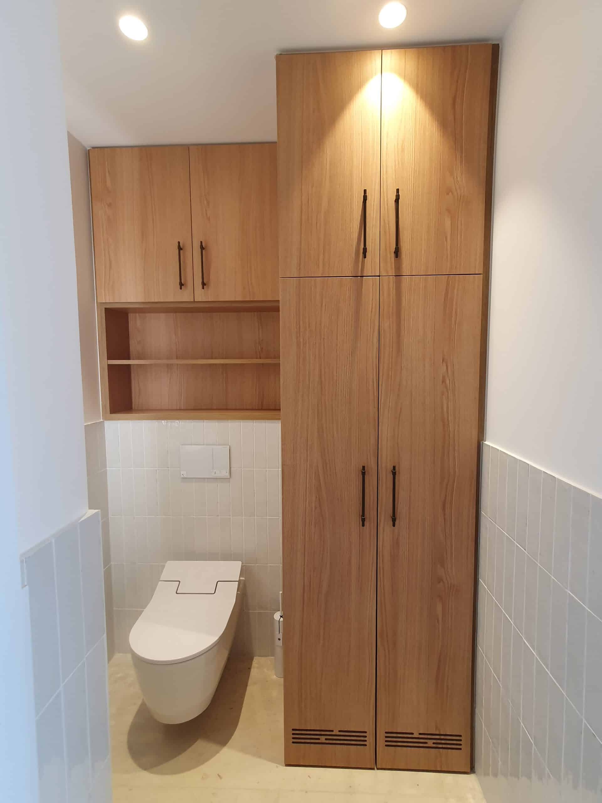 WC suspendu blanc et meubles en bois clair sur carrelage blanc vertical.